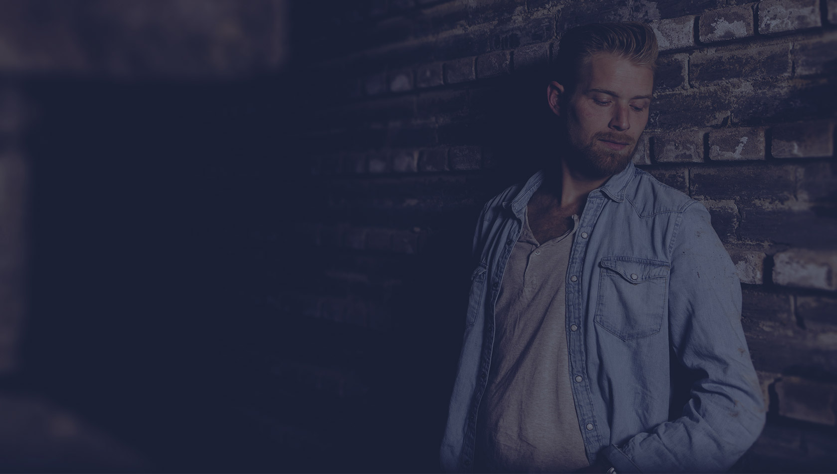 Man in denim shirt leaning against brick wall